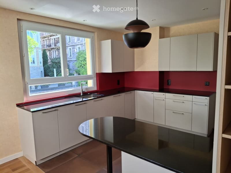 Modern kitchen with white cabinets, red backsplash, black countertop, and a central island with a black table.