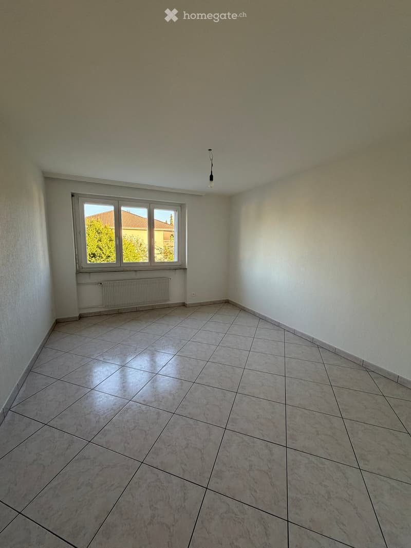Empty room with tiled floor, large window, radiator, and single ceiling light fixture.