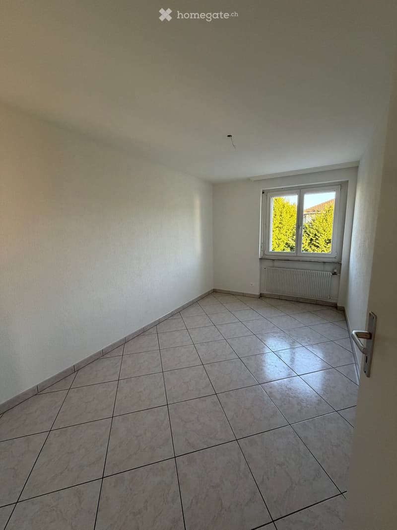 Empty room with tiled floor, white walls, and a window with a radiator below it.