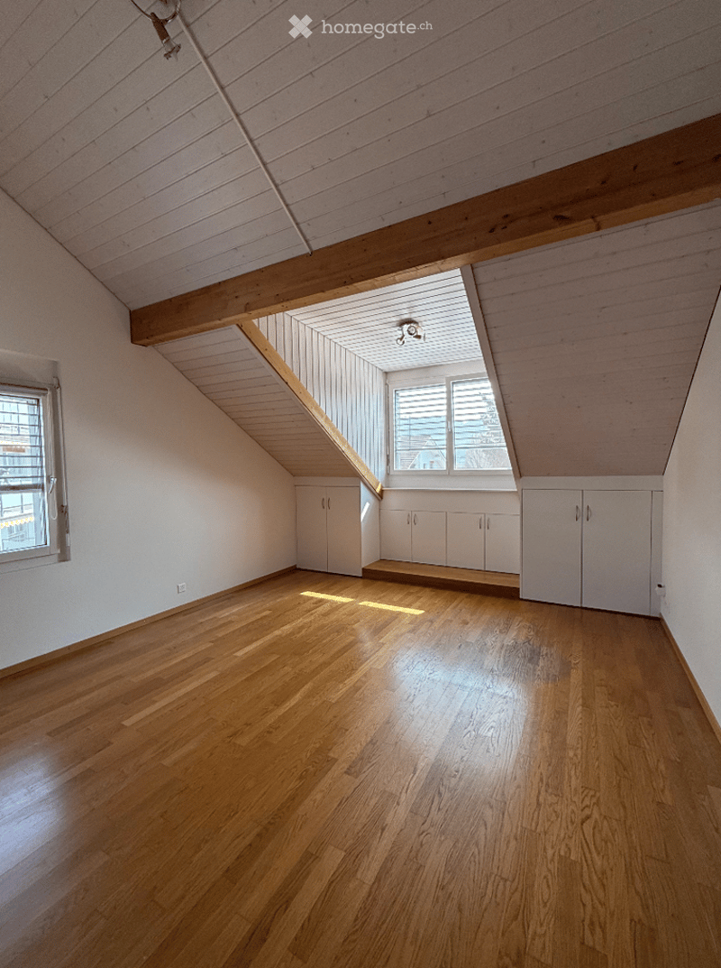 Bright, empty attic room with wooden floors, white walls, built-in cabinets, and skylight windows allowing natural light.