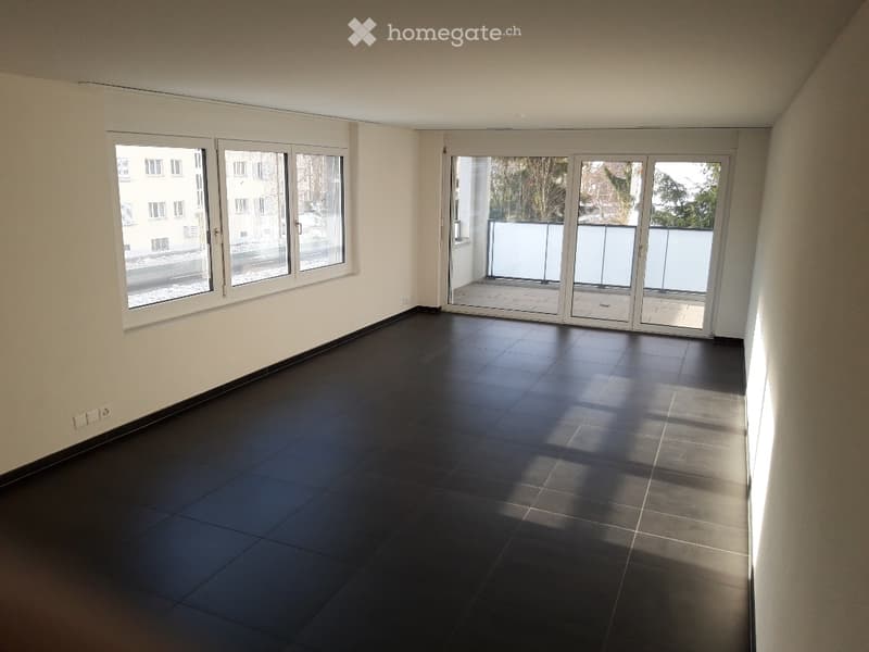 Empty room with dark tiled floor, large windows, and sliding glass doors leading to a balcony.