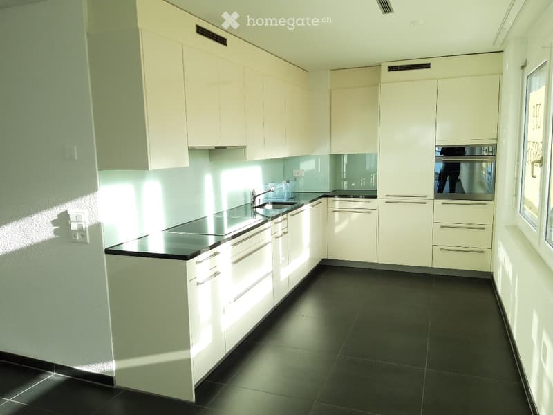Modern kitchen with white cabinets, black countertops, and a built-in oven. Features a sleek design with a dark tiled floor and ample natural light.