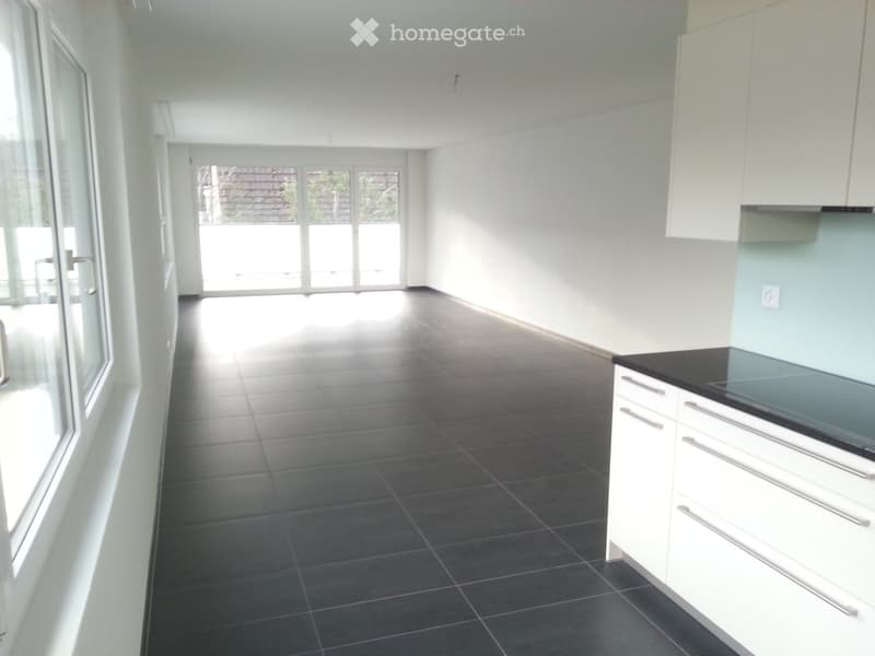 Empty kitchen with white cabinets, black countertop, dark tiled floor, large windows, and glass doors leading to an outdoor area.