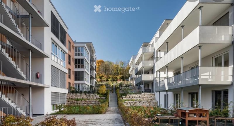 Modern multi-story residential building with balconies, raised ground floor, and landscaped garden area.