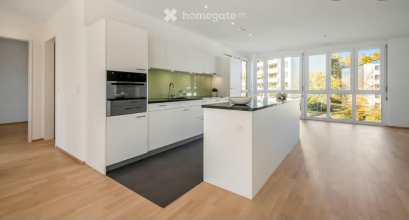 Modern kitchen with white cabinets, black countertops, and a central island. Features include an oven, sink, and ample natural light from large windows.