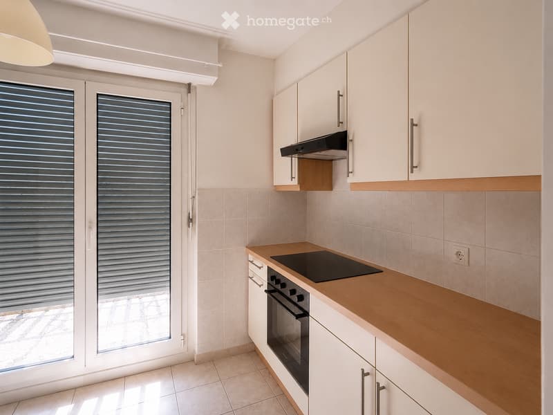 Modern kitchen with white cabinets, wooden countertops, induction stove, and oven. Large window with blinds provides natural light.