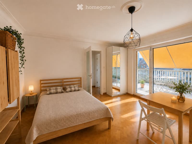 Bright bedroom with wooden flooring, a bed with plaid pillows, a nightstand with a lamp, a small table with chairs, a mirror, and a wicker basket with a plant on top of a wooden cabinet.