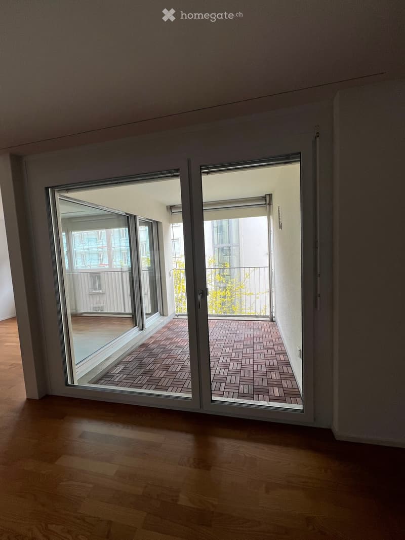 Empty room with wooden flooring and large sliding glass doors leading to a balcony with brick tiles.