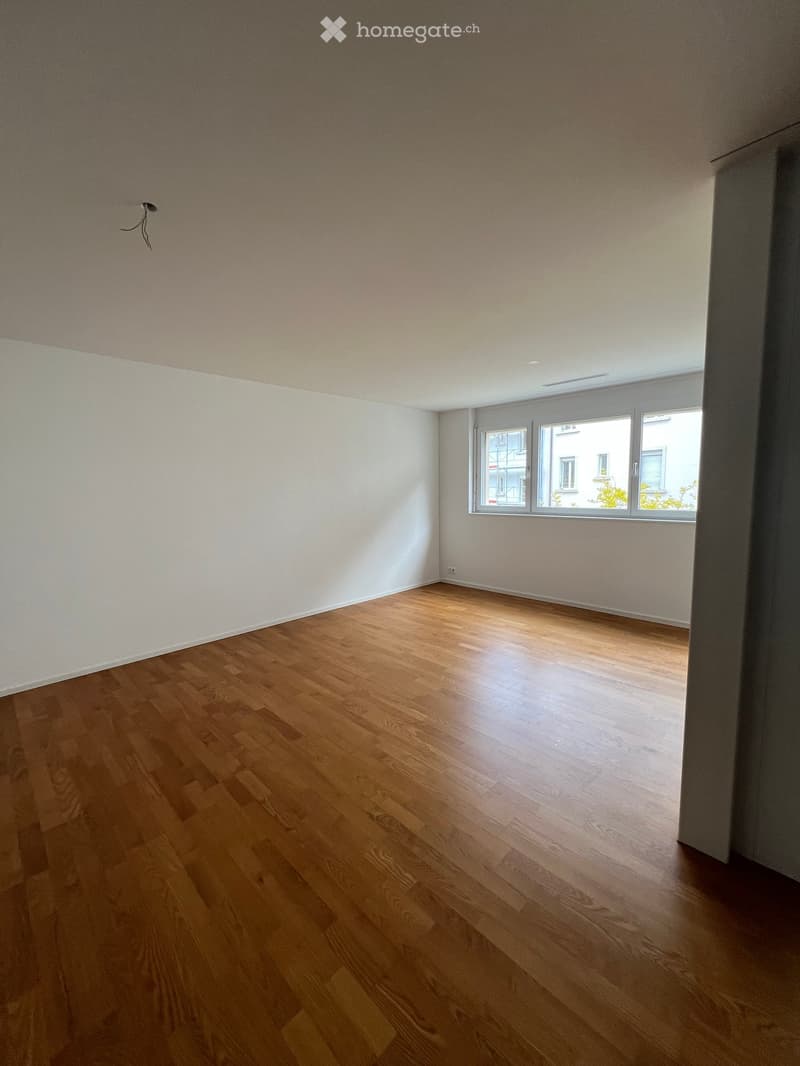 Empty room with wooden flooring and white walls, featuring large windows with a view of the outside.