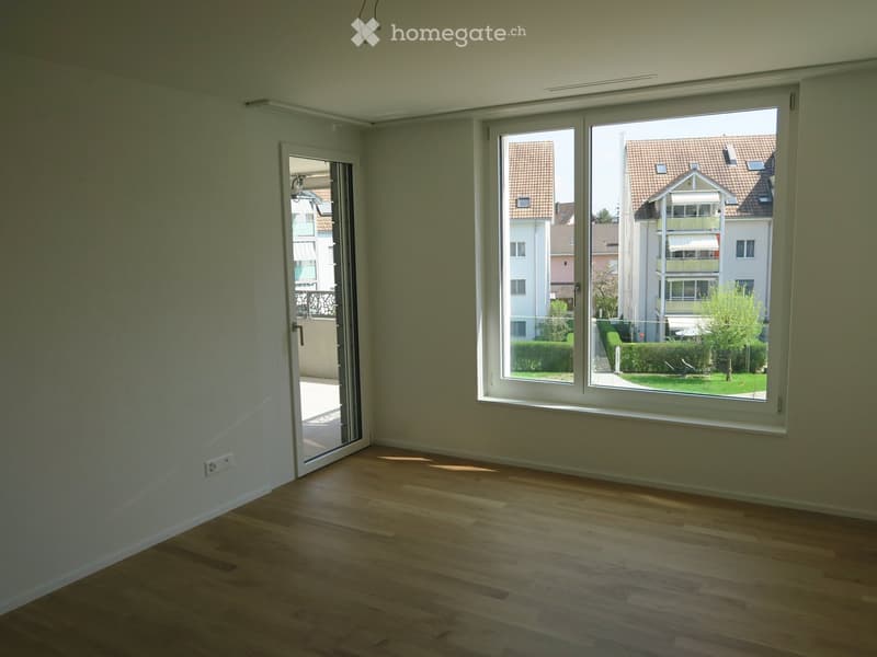 Empty room with wooden flooring, large window, and sliding glass door leading to a balcony.