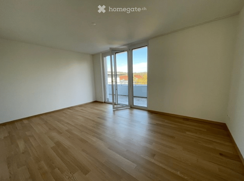 Empty room with wooden flooring, white walls, and large sliding glass doors leading to a balcony.