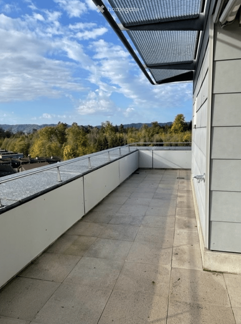 Modern rooftop terrace with clean lines, white walls, and a panoramic view of the city and surrounding landscape.