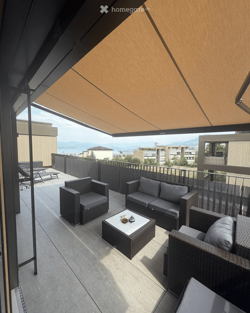 Balcony with a view, featuring a sofa, chairs, a coffee table, and a small table with items on it.