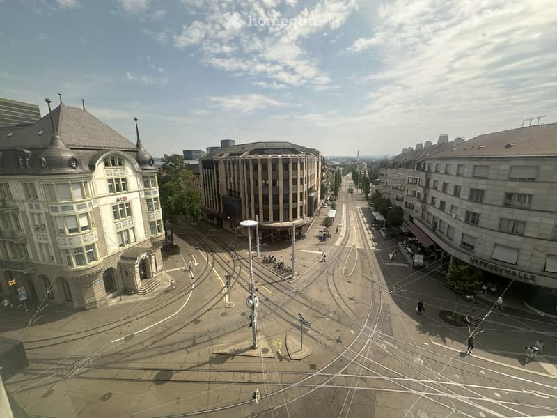 Aerial view of a city street intersection with tram tracks, buildings, and pedestrians.
