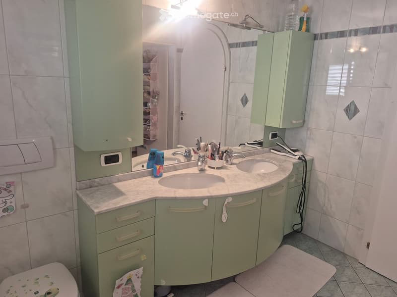Modern bathroom with a double sink vanity, light green cabinets, marble countertop, and a large mirror above the sinks.