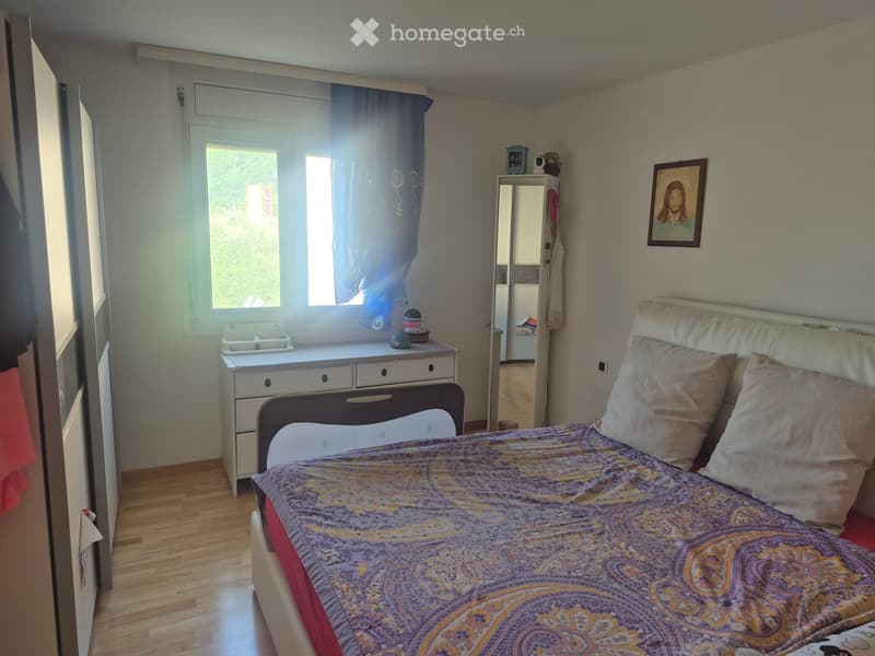 Cozy bedroom with a double bed, nightstand, mirror, and a small desk near the window. The room features wooden flooring and a framed picture on the wall.