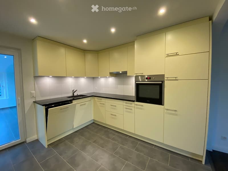Modern kitchen with light-colored cabinets, black countertops, and stainless steel appliances including an oven and dishwasher.