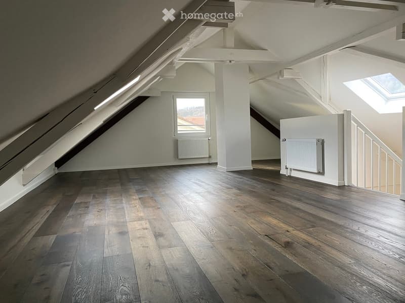 Empty attic space with wooden flooring, white walls, exposed wooden beams, skylight windows, and a staircase leading to another level.