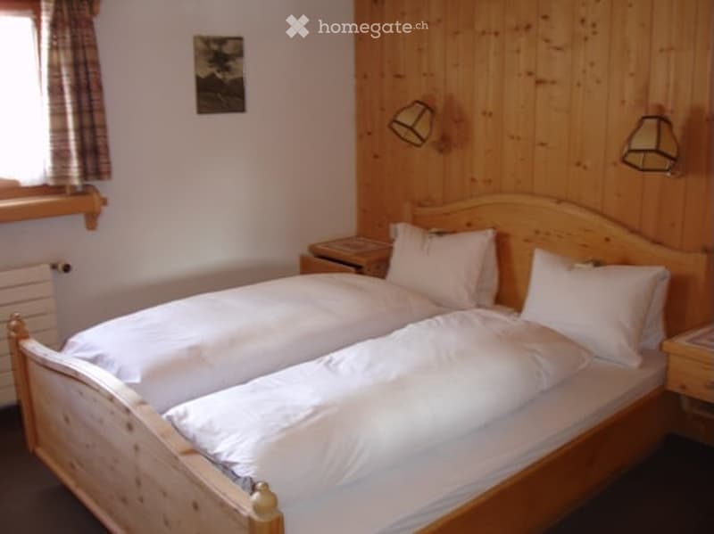 Cozy bedroom with wooden walls, a large double bed with white bedding, nightstands, and wall-mounted lamps.