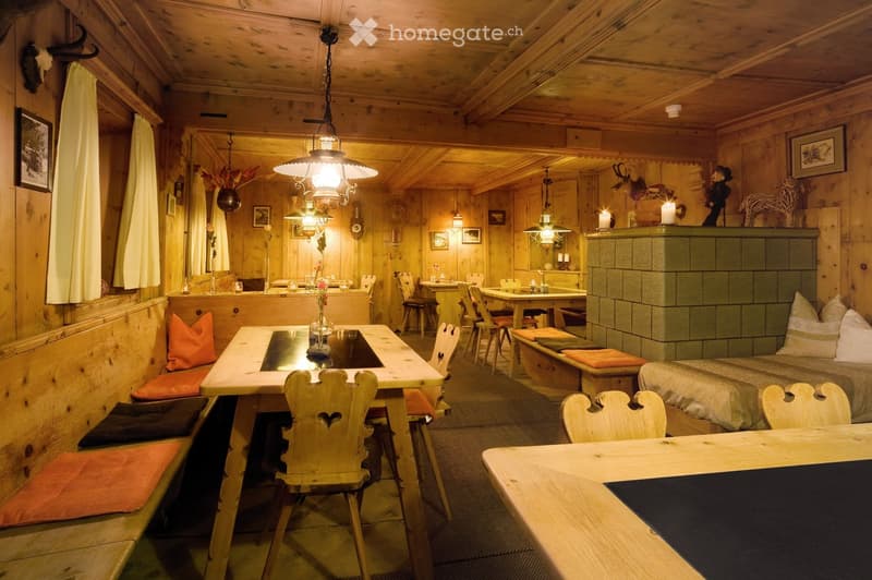 Cozy wooden-paneled room with a dining table, chairs, sofa, and decorative items including candles and artwork.