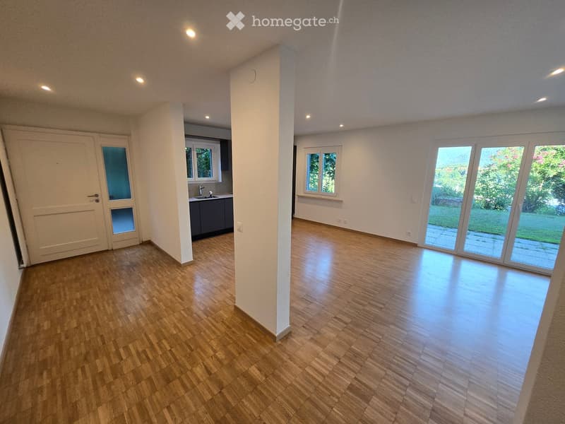 Empty room with wooden flooring, white walls, and large windows, including a sliding glass door leading to an outdoor area.