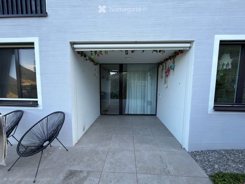 Outdoor patio area with tiled floor, two black wire chairs, and a view of the house entrance with a retractable awning and floral decorations.