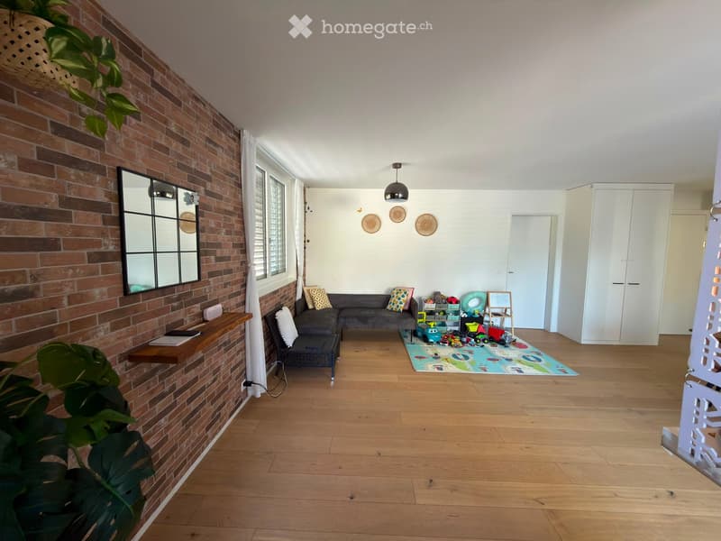 Living room with exposed brick wall, wooden floor, sofa, chair, small table, mirror, and toys on the floor.