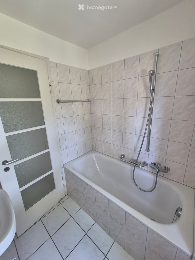 Bathroom with a bathtub, shower hose, and a frosted glass door.