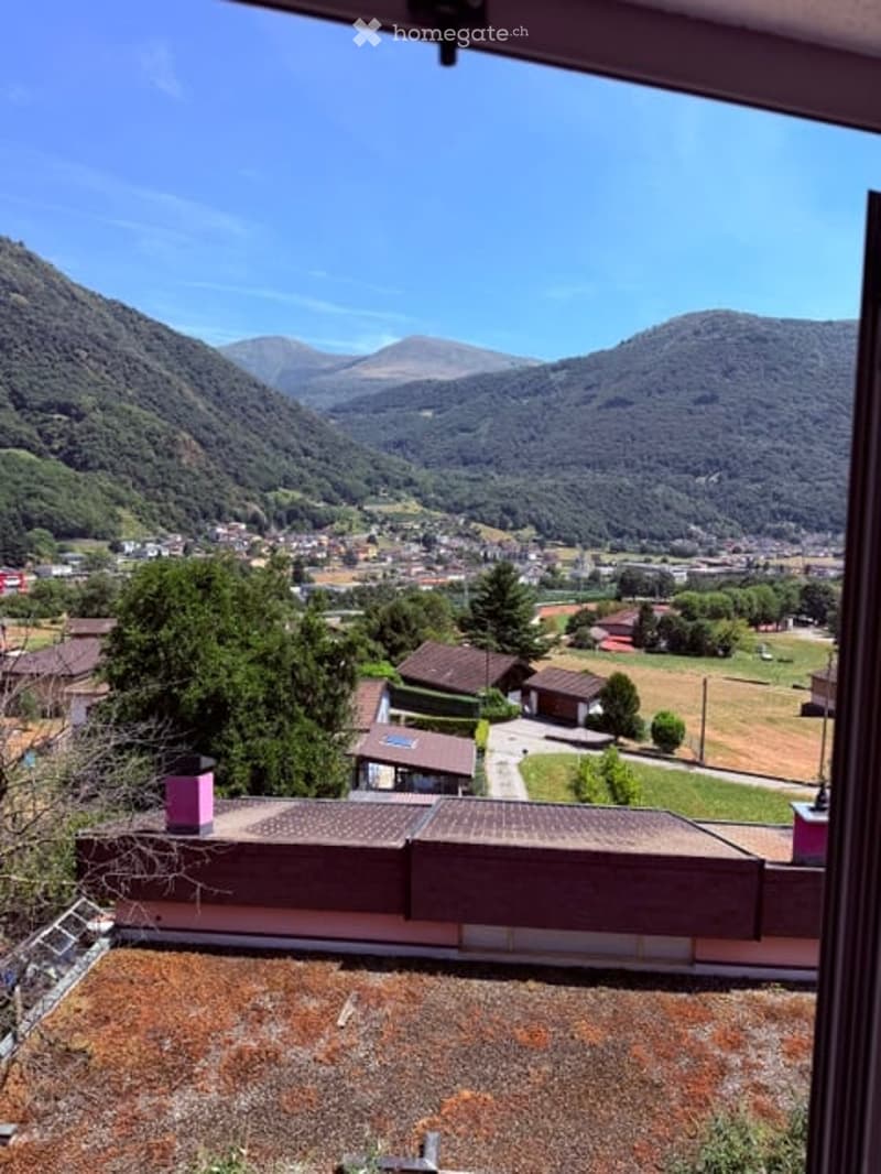 View from a balcony or terrace overlooking a town nestled in a valley with surrounding mountains.