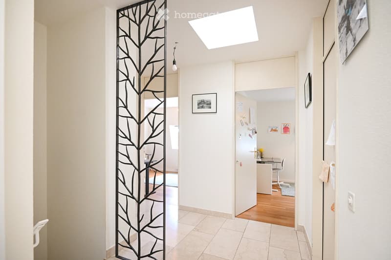 Bright hallway with white walls, tiled floor, and modern decor including a tree-shaped metal screen, framed artwork, and a pendant light fixture.