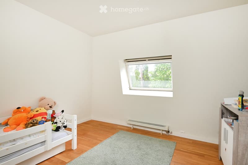 A small, well-lit bedroom with a white bunk bed, stuffed toys, a grey rug, and a small cabinet with books and items on top.