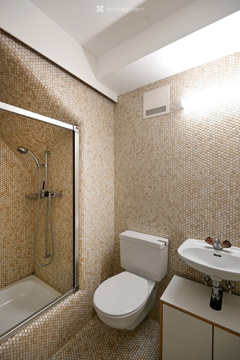 Modern bathroom with a white toilet, sink, bathtub, and showerhead. The walls and floor are covered in a circular patterned tile.