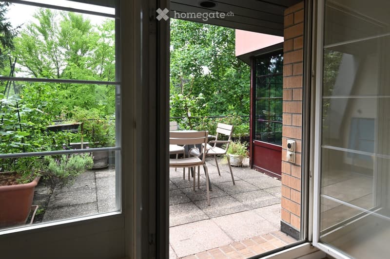 Balcony with a table and chairs, surrounded by greenery and potted plants, with a view of the garden.