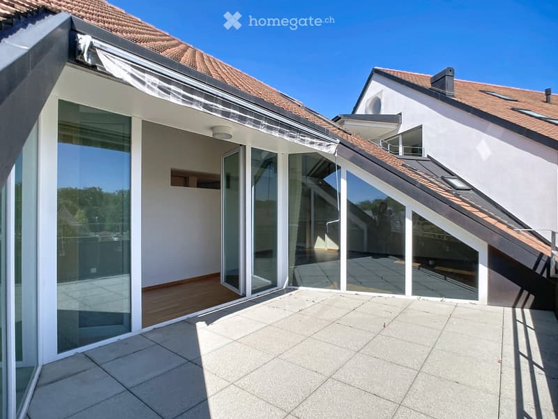 Modern balcony with large glass sliding doors, concrete floor, and a view of the house exterior with a tiled roof and white walls.