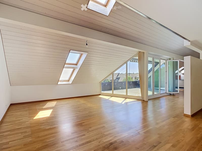 Bright, empty room with wooden flooring and white paneled walls, featuring large skylights and a set of sliding glass doors leading to an outdoor area.