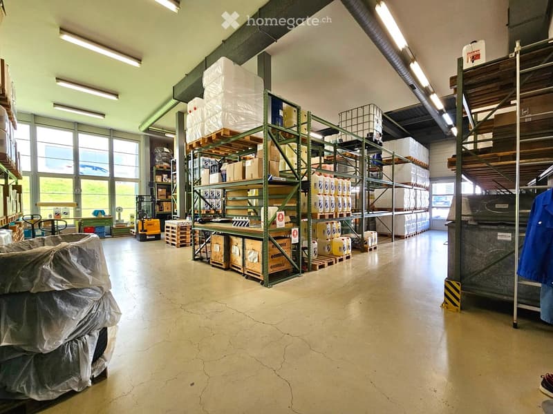 Warehouse with metal shelving units filled with boxes, barrels, and pallets. A forklift is visible near the shelves, and a work table is positioned in the foreground.