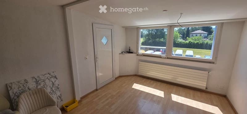 Empty room with wooden flooring, large window, radiator, and a single sofa in the corner.