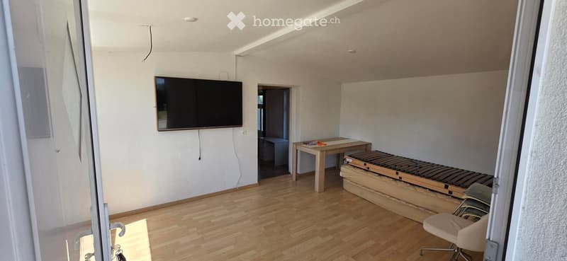 A modern living room with a wooden floor, a mounted screen on the wall, a small table, and a chair.