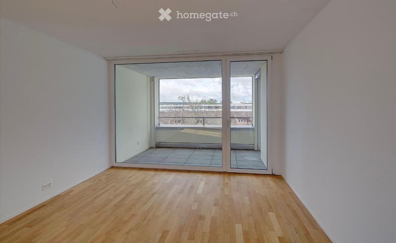 Empty room with wooden flooring, white walls, and large sliding glass doors leading to a balcony.