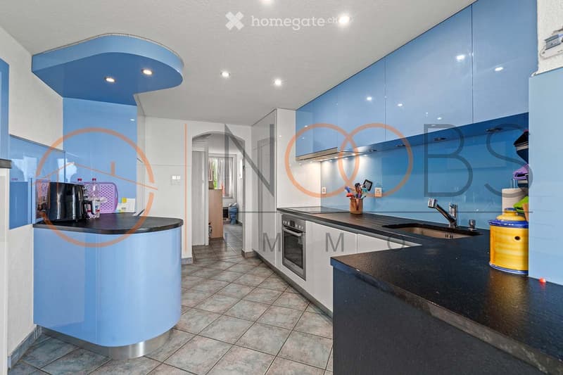 Modern kitchen with light blue cabinets, black countertops, stainless steel appliances, and a central island.