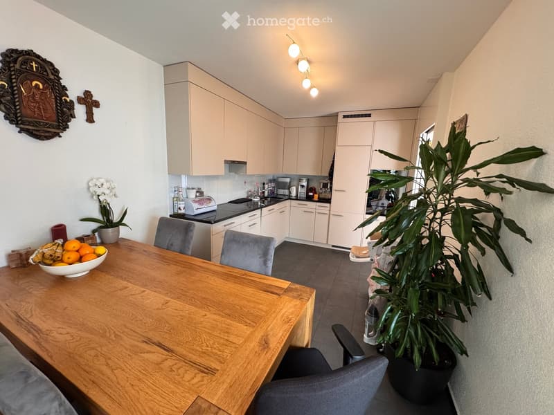 A modern kitchen and dining area with a wooden dining table, grey chairs, light-colored cabinets, and various appliances.