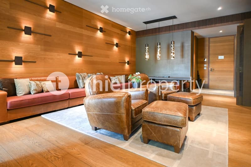 Modern living room with wooden walls, leather furniture including a sofa, armchairs, and ottomans, a small table with a flower vase, and pendant lights.