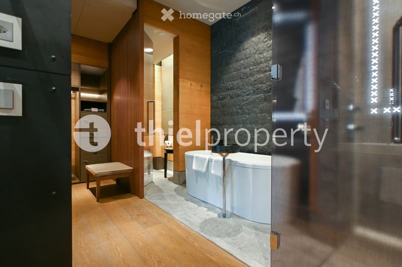 Modern bathroom with a freestanding bathtub, wooden stool, built-in cabinet, and sleek glass shower enclosure.