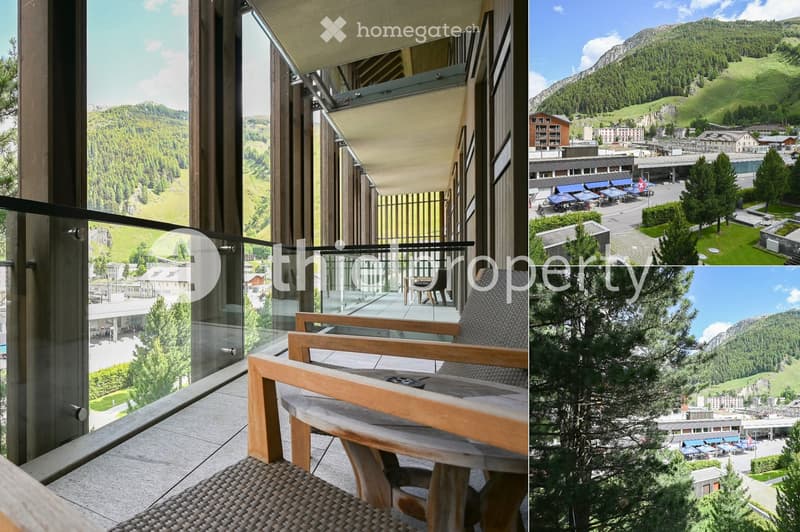 Balcony with a wooden table and chairs, overlooking a scenic mountain landscape and town.