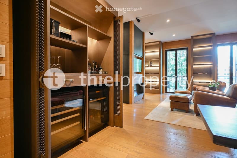 Modern living room with wooden flooring, large windows, leather sofa, coffee table, armchair, ottoman, wine rack, and built-in cabinetry.