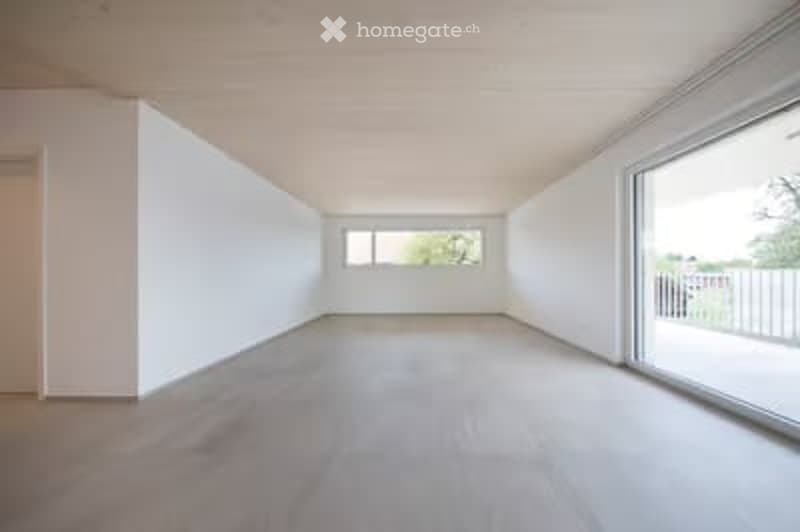 Completely empty room with white walls, wooden floor, large window, and sliding glass door leading to a balcony.