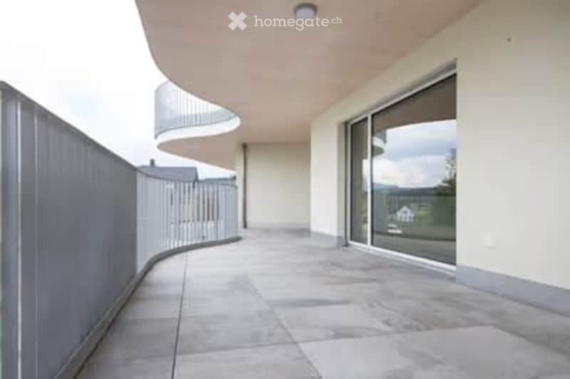 Modern balcony with large glass sliding doors, tiled floor, and a curved railing.