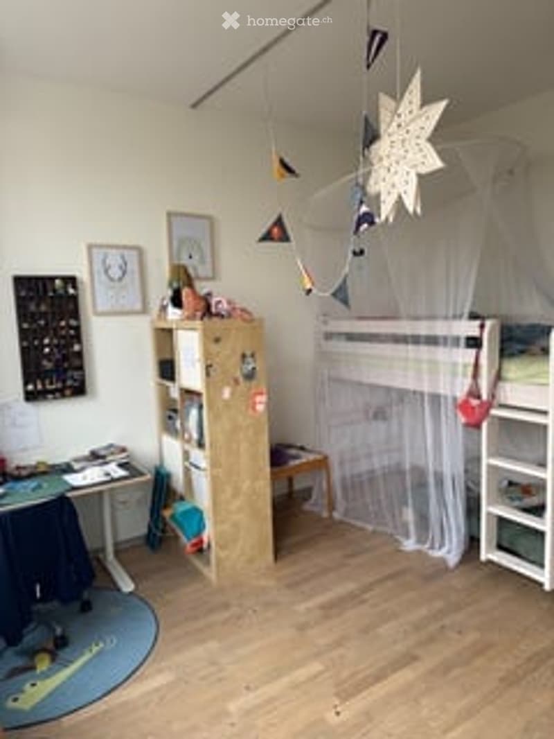 A child's bedroom with a lofted twin-sized bed, a small bookshelf, a table, and a colorful play mat on the floor.