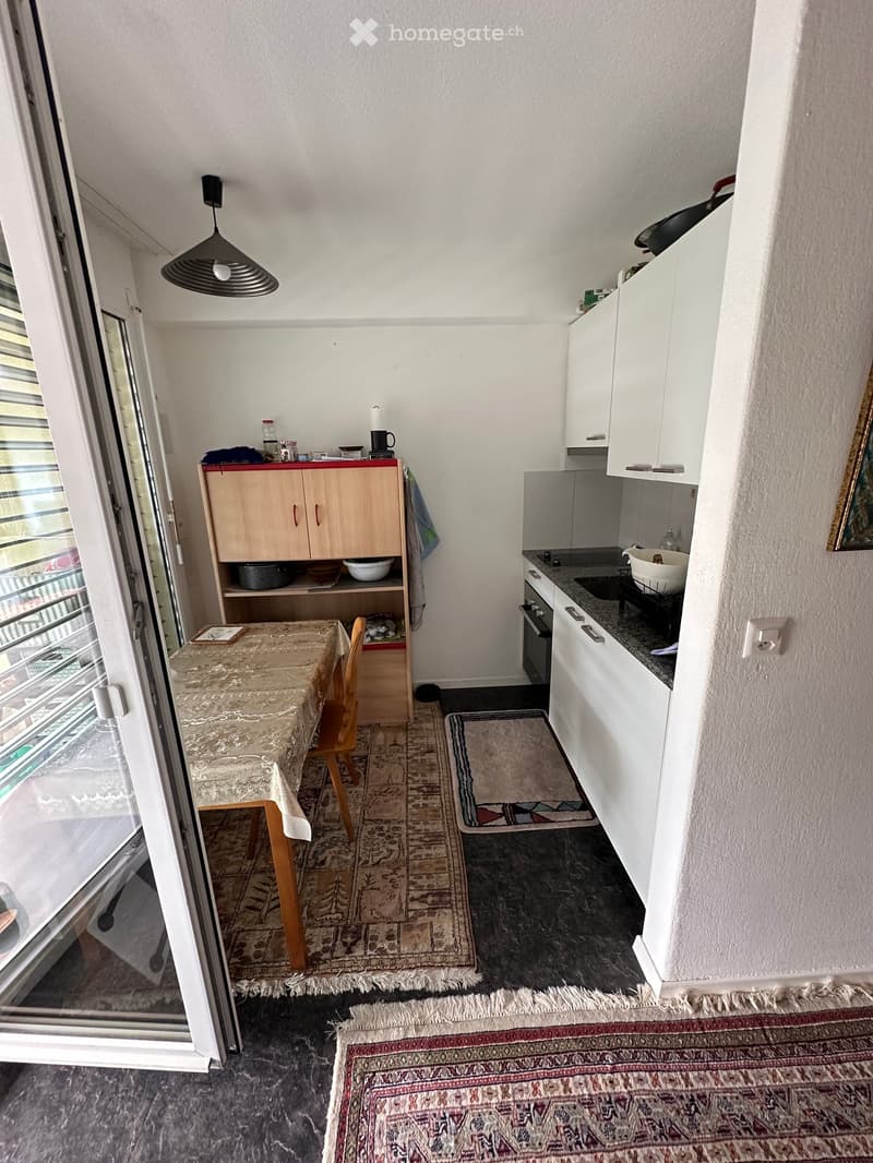 A compact, well-lit kitchen and dining area with white cabinets, a small dining table with a chair, and various kitchen appliances.