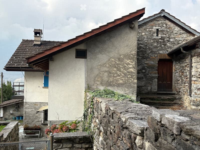 Traditional stone and plaster exterior, red tiled roof, wooden door, blue shutters, garden with greenery and a white bench